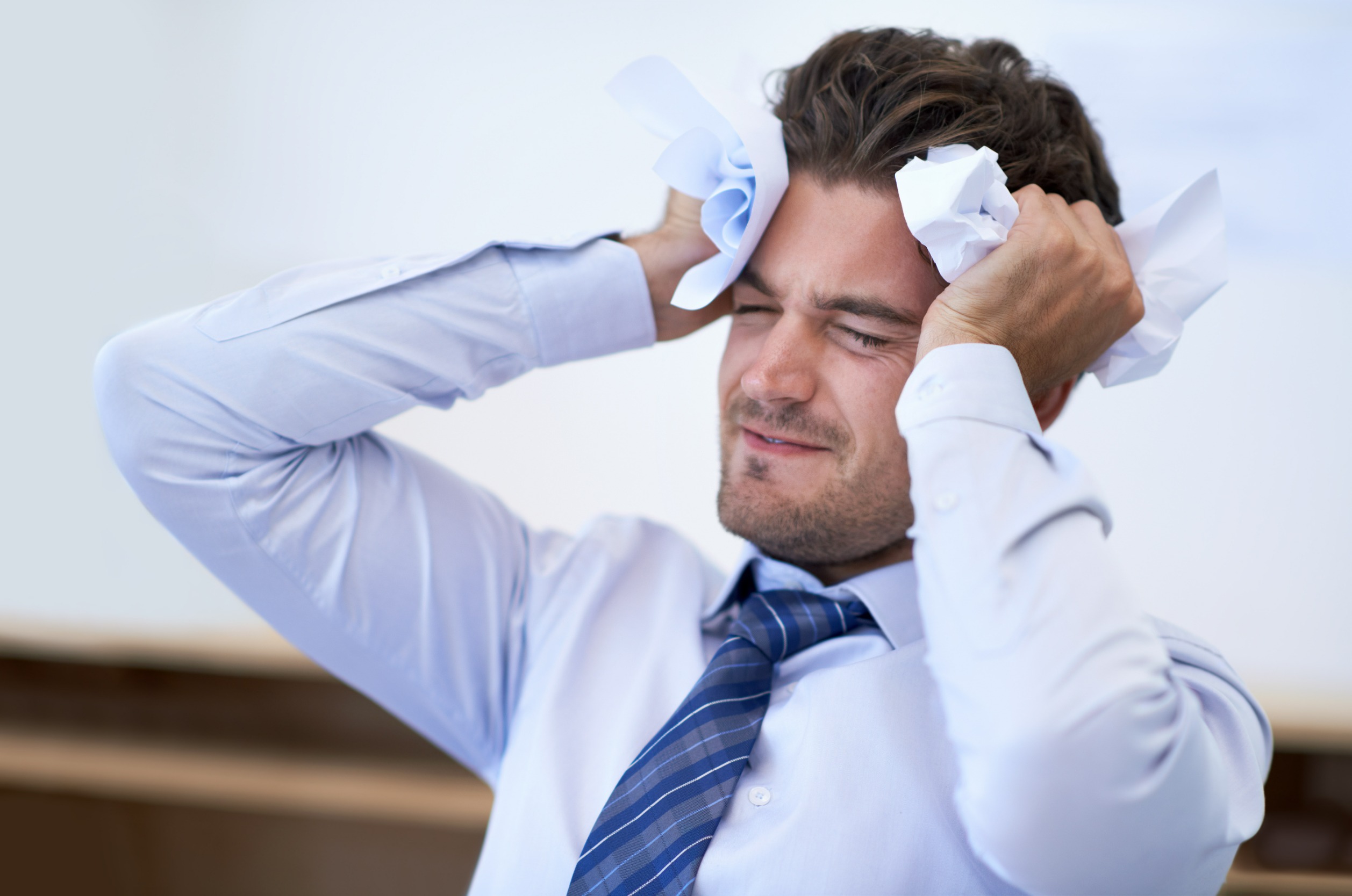 A man sitting with his hands on his head, looking distressed and suffering from a headache due to stress.